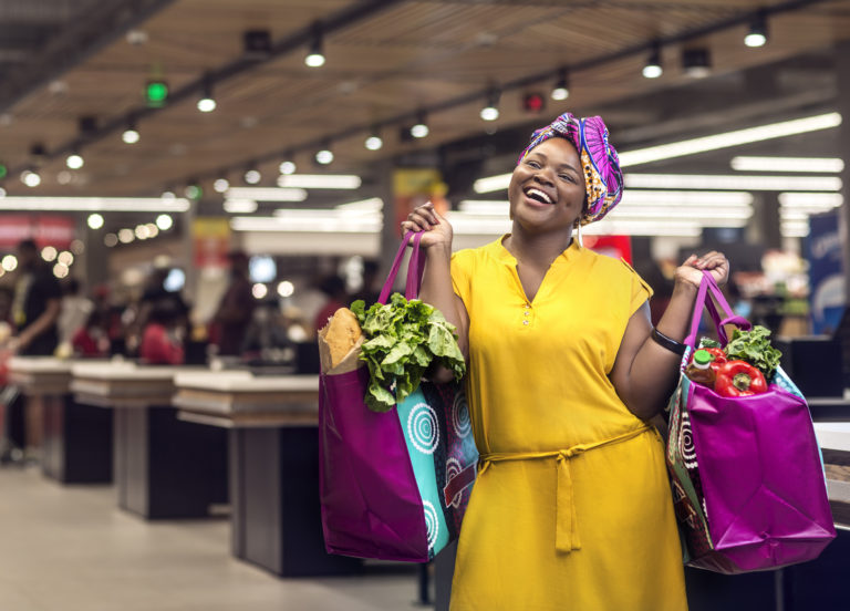 Rapariga Moçambicana, com uma linda capulana à cabeça, carrega alegremente dois sacos de compras com vegetais no Baía Mall em Maputo, para a campanha publicitária do Millennium BIM Dobra Mola.