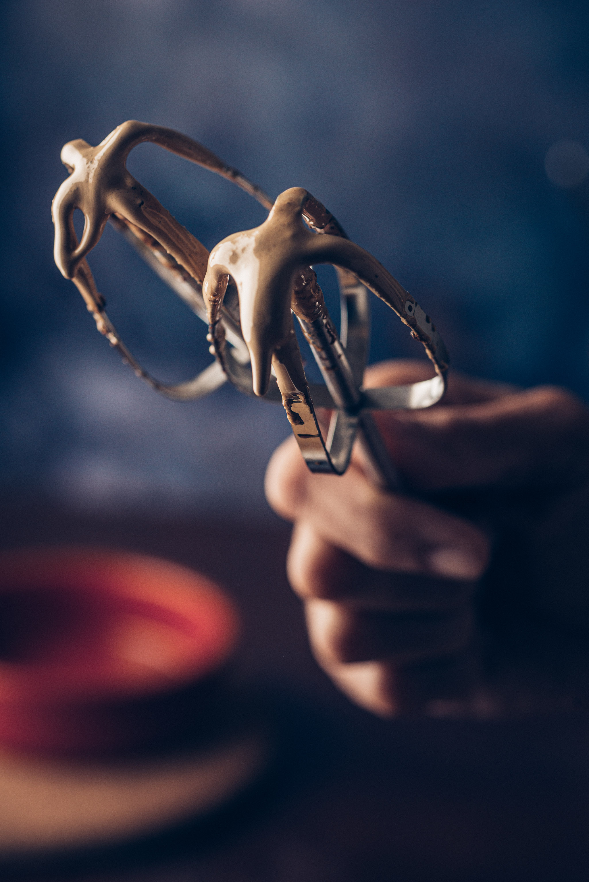Hand holding two electric mixer beaters coated in freshly whipped dalgona coffee.