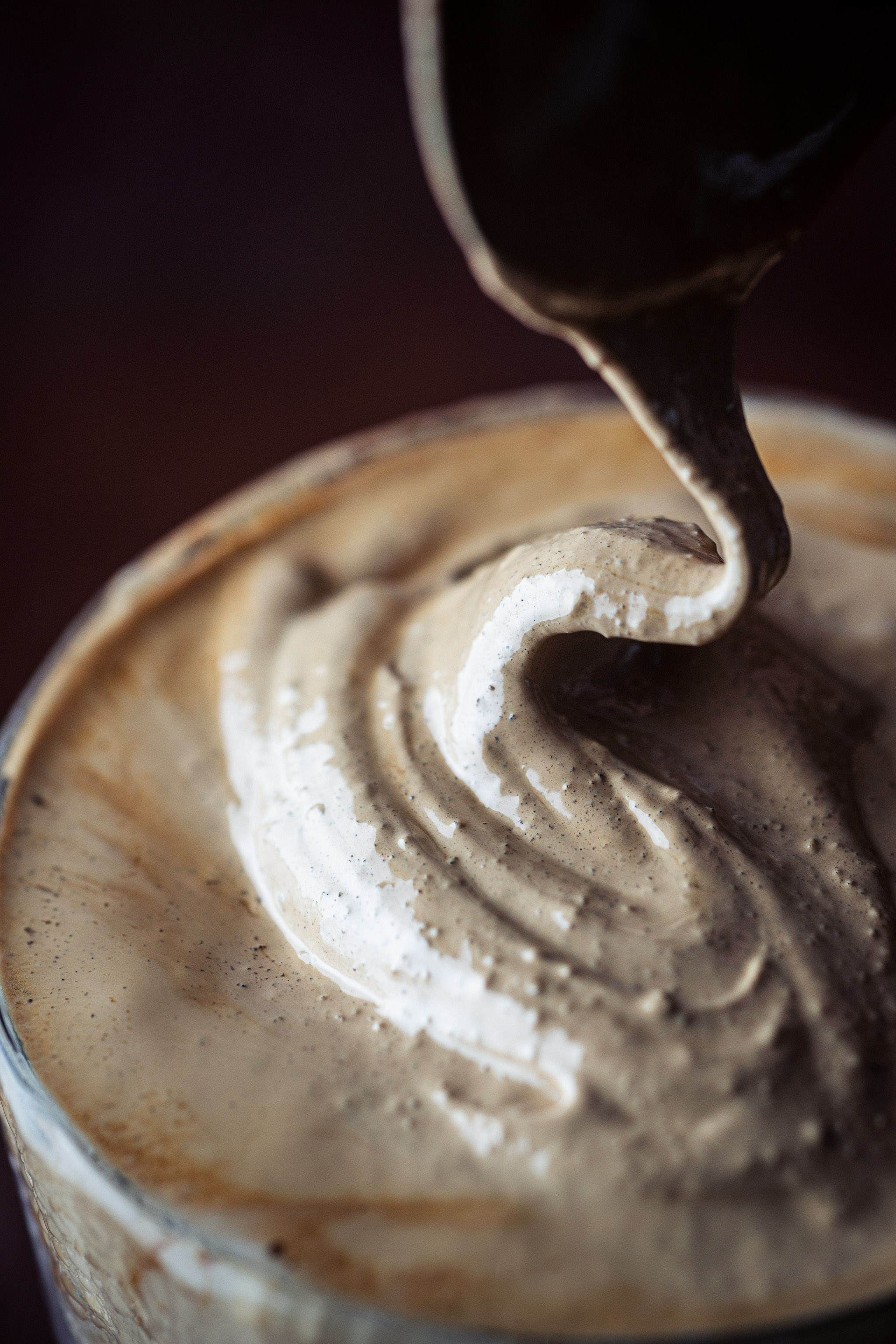 Whipped dalgona coffee forming a soft, wave-like peak on top of a glass of iced milk.