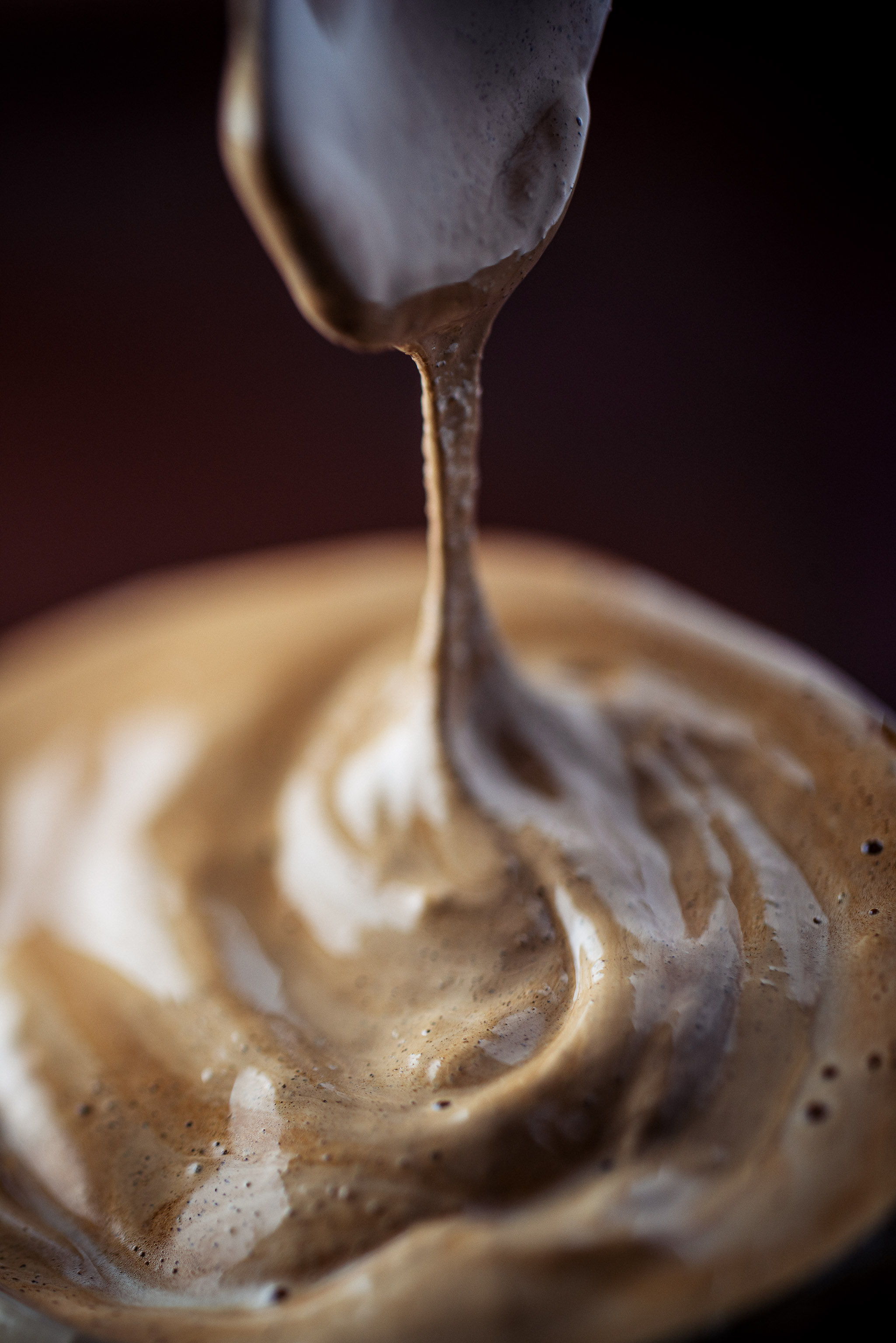 Close-up of creamy whipped dalgona coffee forming soft peaks as it drips from a spoon.